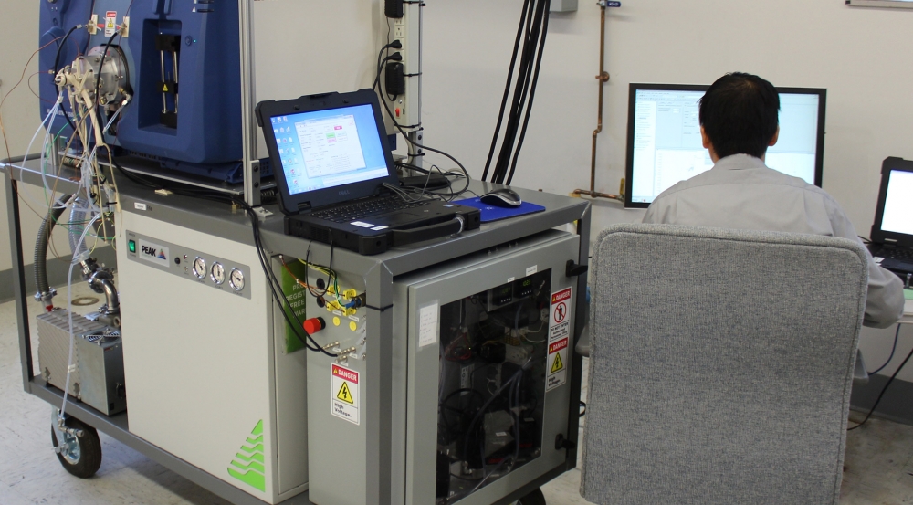 A researcher sits a monitor next to a mass spectrometer as it conducts measurements.