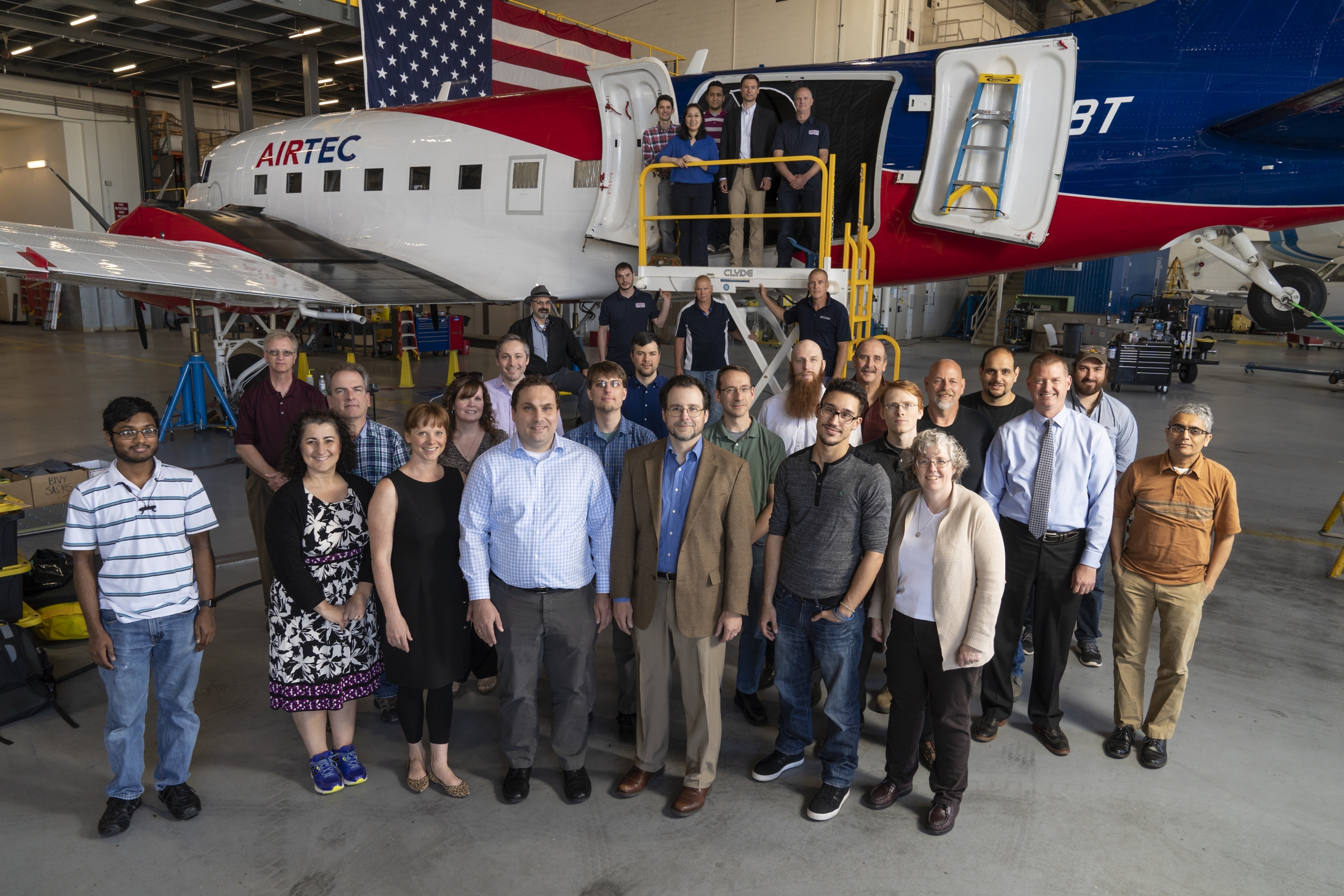 A group of about 30 people pose in front of an airplane