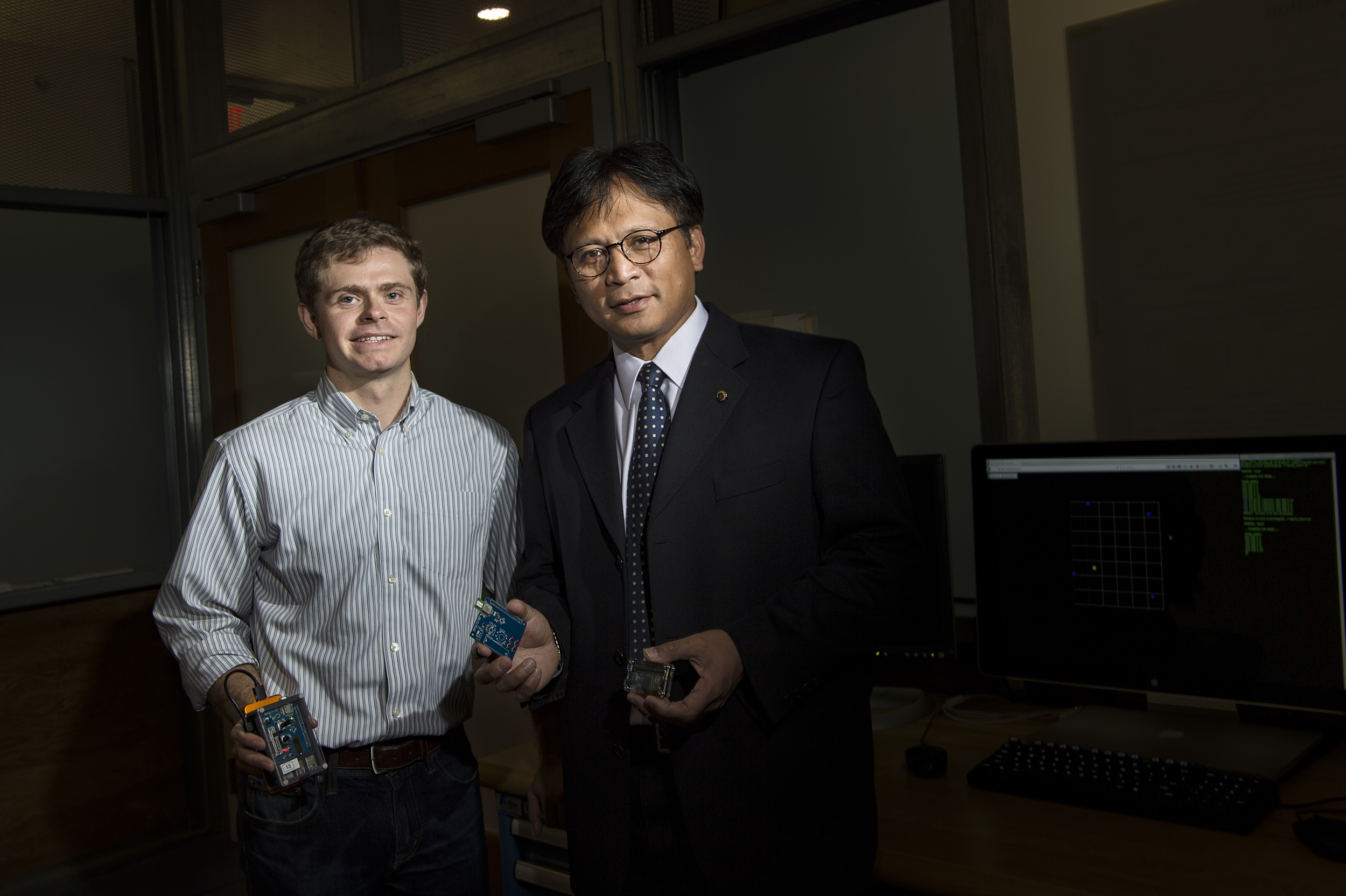 Two researchers pose for a photo in lab holding a small electronic device 