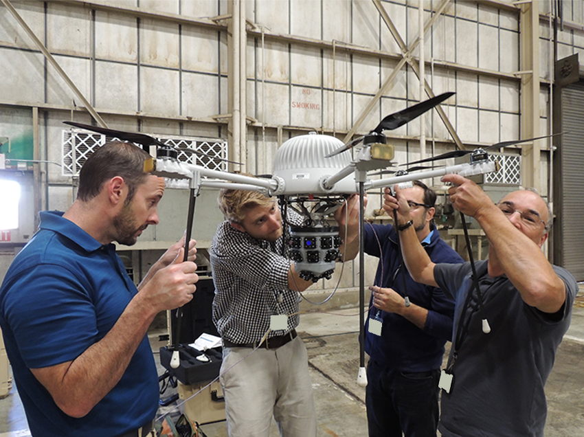 Four people holding up a drone as they work on it.
