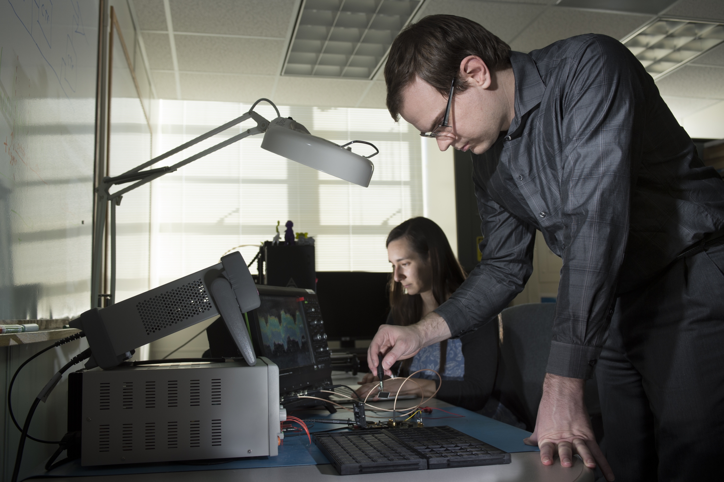 A photo of two staff members with electronic equipment in front of them in a lab