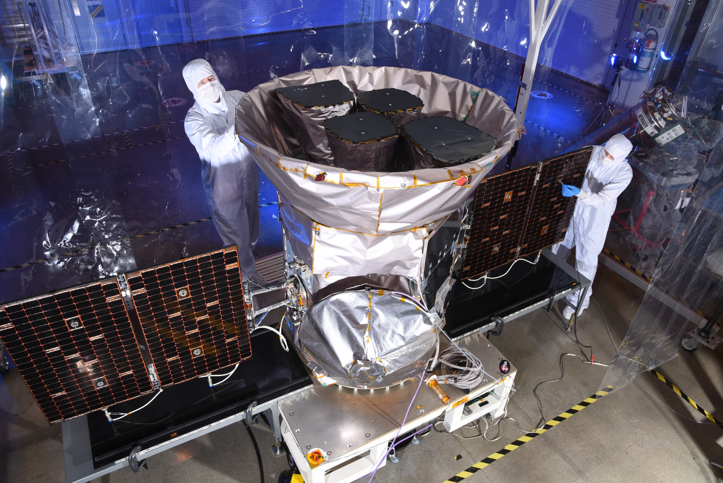 A photo of two scientists inspecting the tess satellite in a cleanroom environment. 