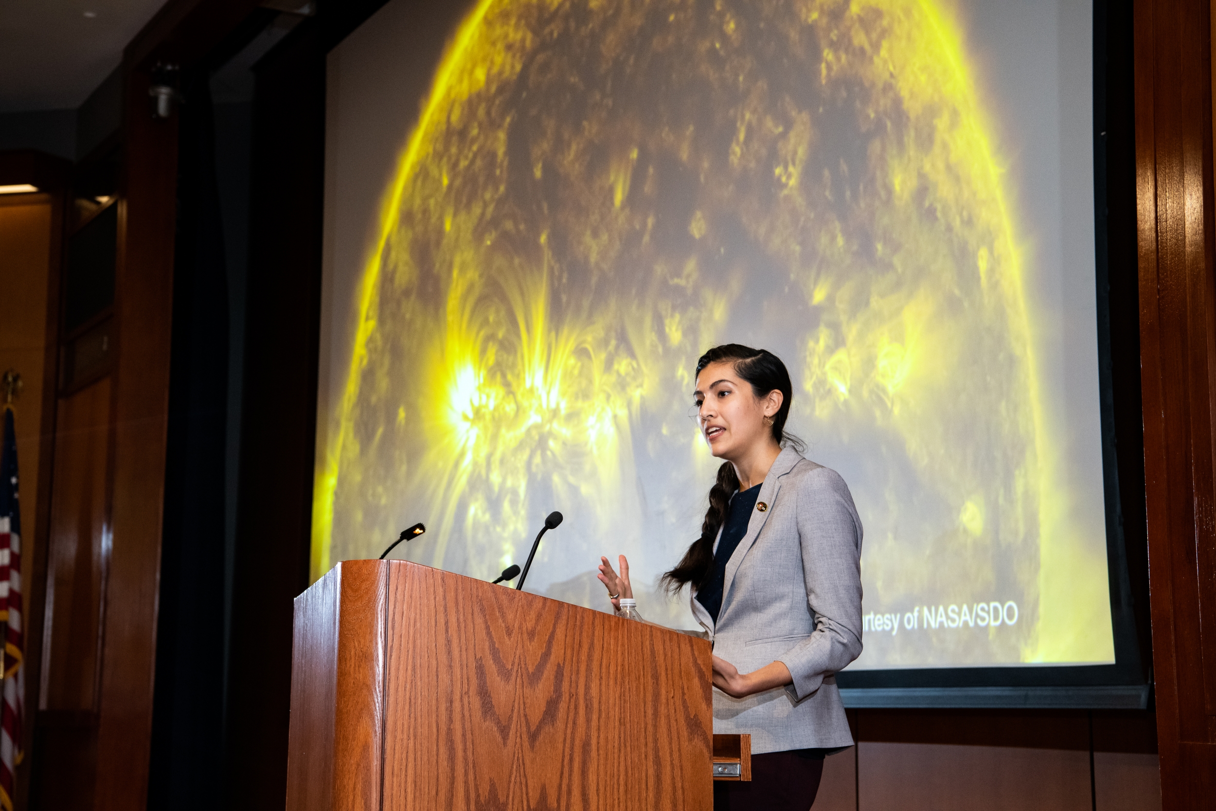 Natalia Guerrero stands at the lecturn and gives her keynote speech in front of a large image of a sun