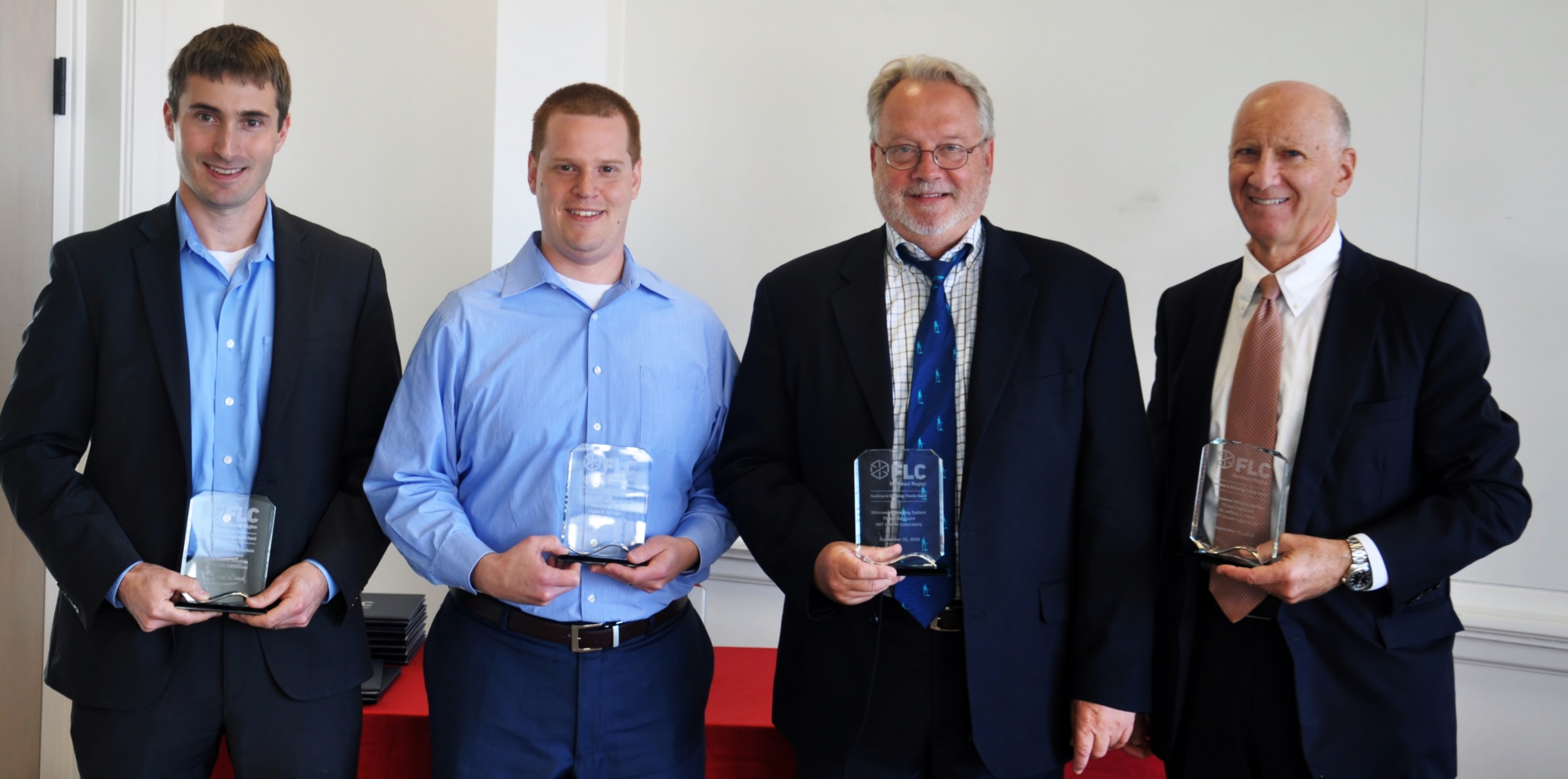 Four lincoln laboratory staff members stand each holding a glass award. 