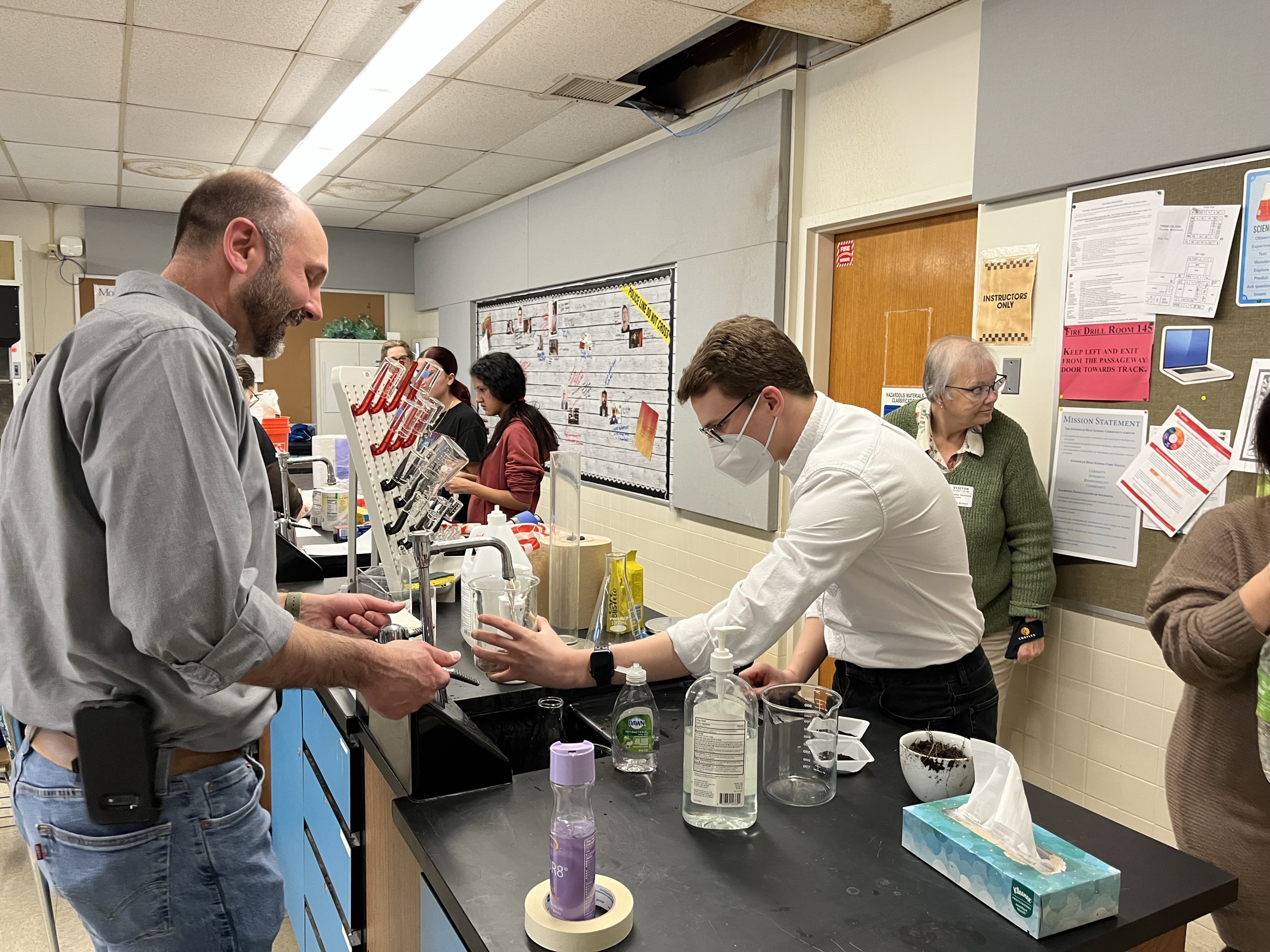 Two instructors in a classroom to fill a beaker with water.