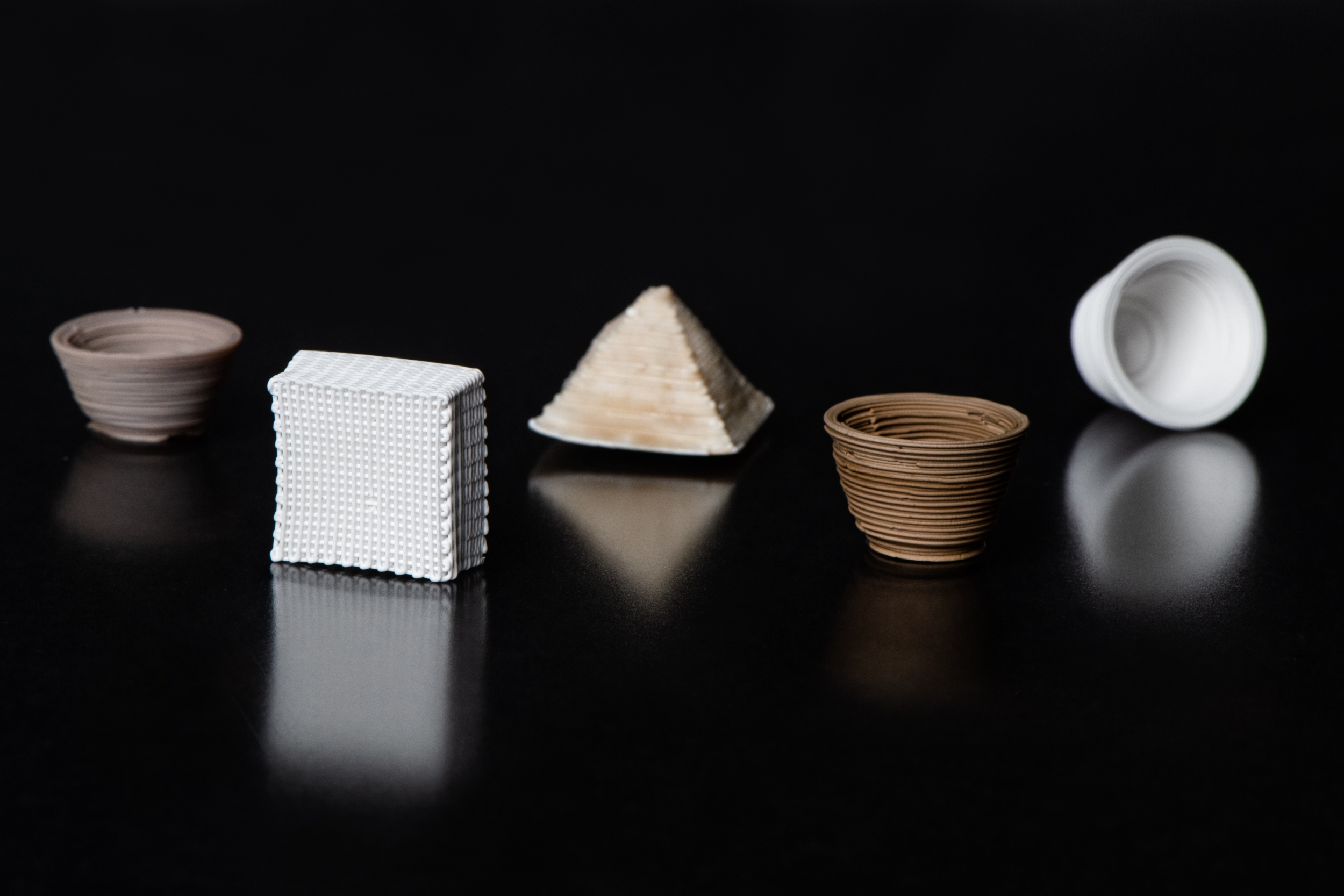 Five small 3D-printed vessels of various colors (white, browns) and shapes (cups, pyramid shapes