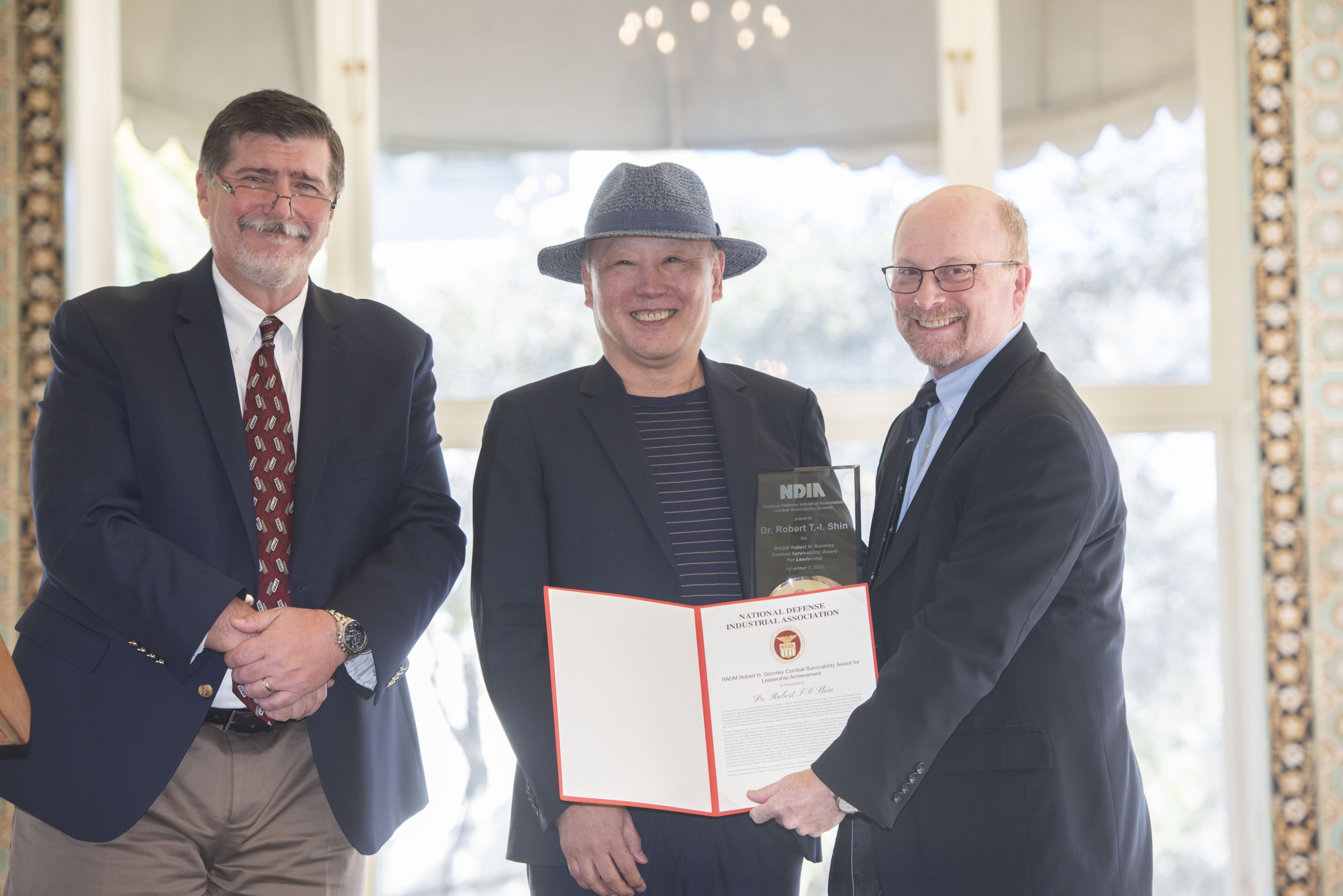 An awardee holds an award plaque next to two award presenters. 