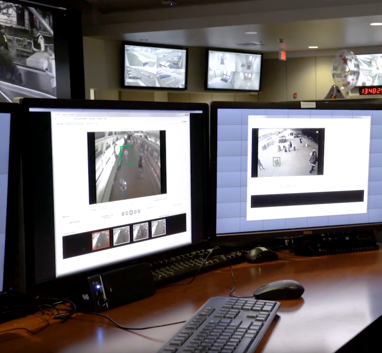 Two desktop monitors run software for forensic video analysis, with two additional monitors in the background capturing video surveillance from different angles. 