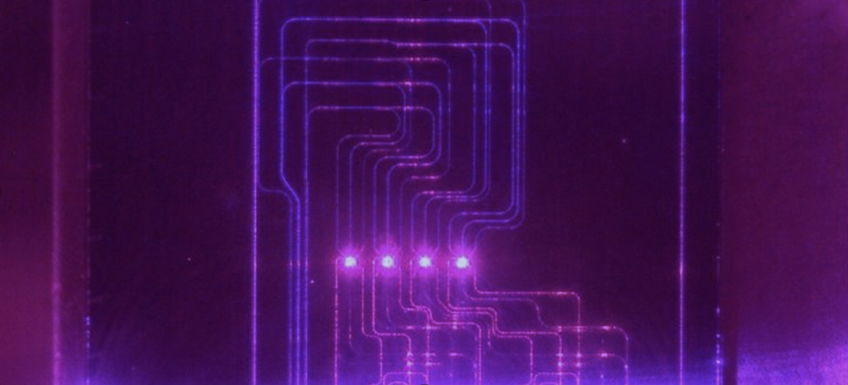 Optical microscope image of chip simultaneously illuminated with 7 wavelengths from 405–1092 nm, fabricated using the silicon nitride and alumina visible light platform (370–1100 nm)​.