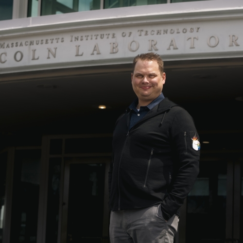 A portrait photograph of Joshua Van Hook outside the front entrance of MIT Lincoln Laboratory.