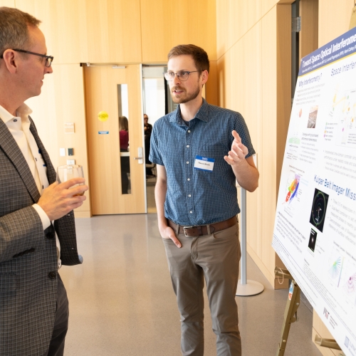 Laboratory staff member Mason Black gestures while presenting a poster of his work to a luncheon attendee.