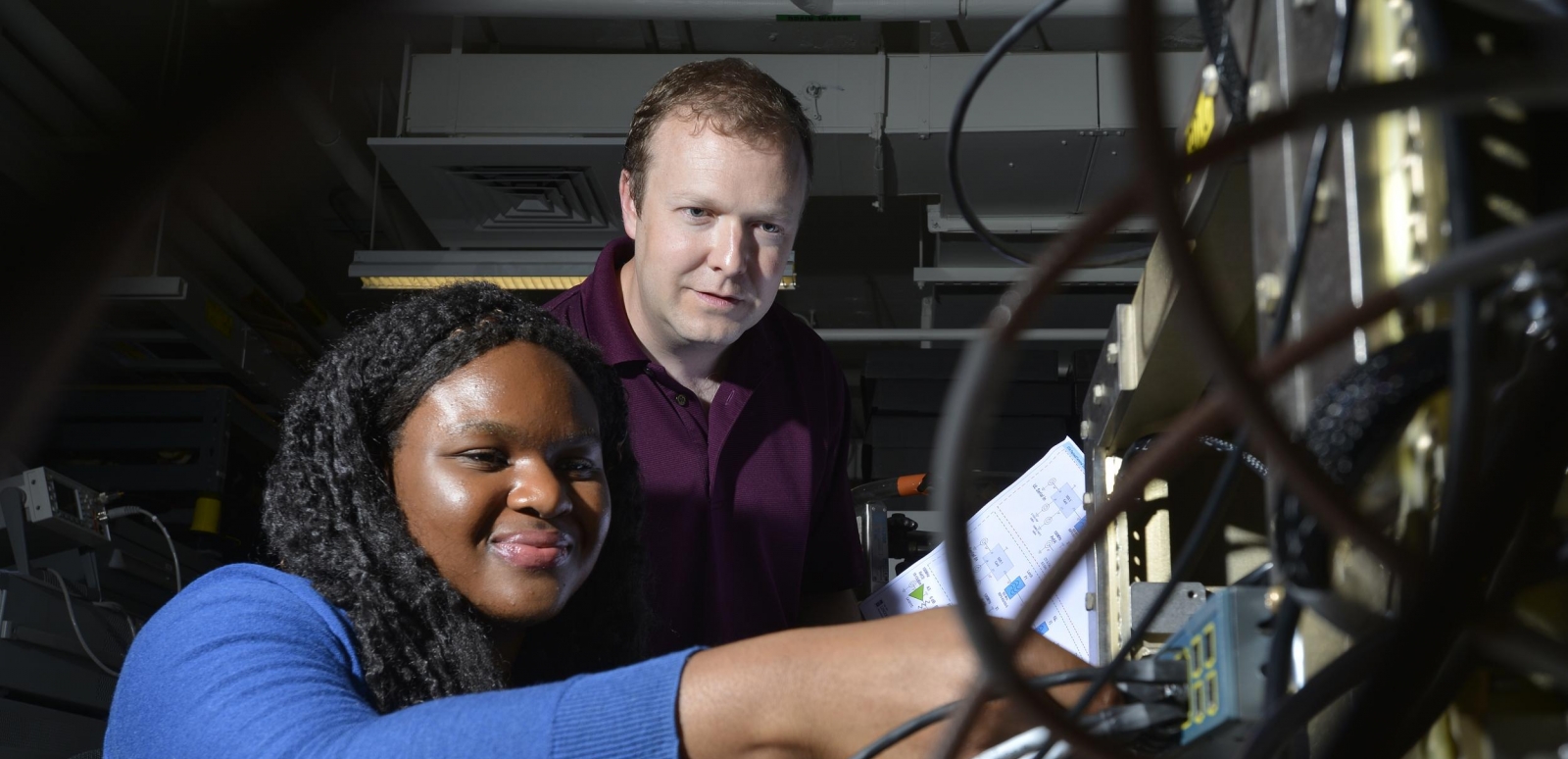 Derrick Feld looks on as AFCEA intern Chi-chi Nwodoh connects wires on the test terminal she helped build. 