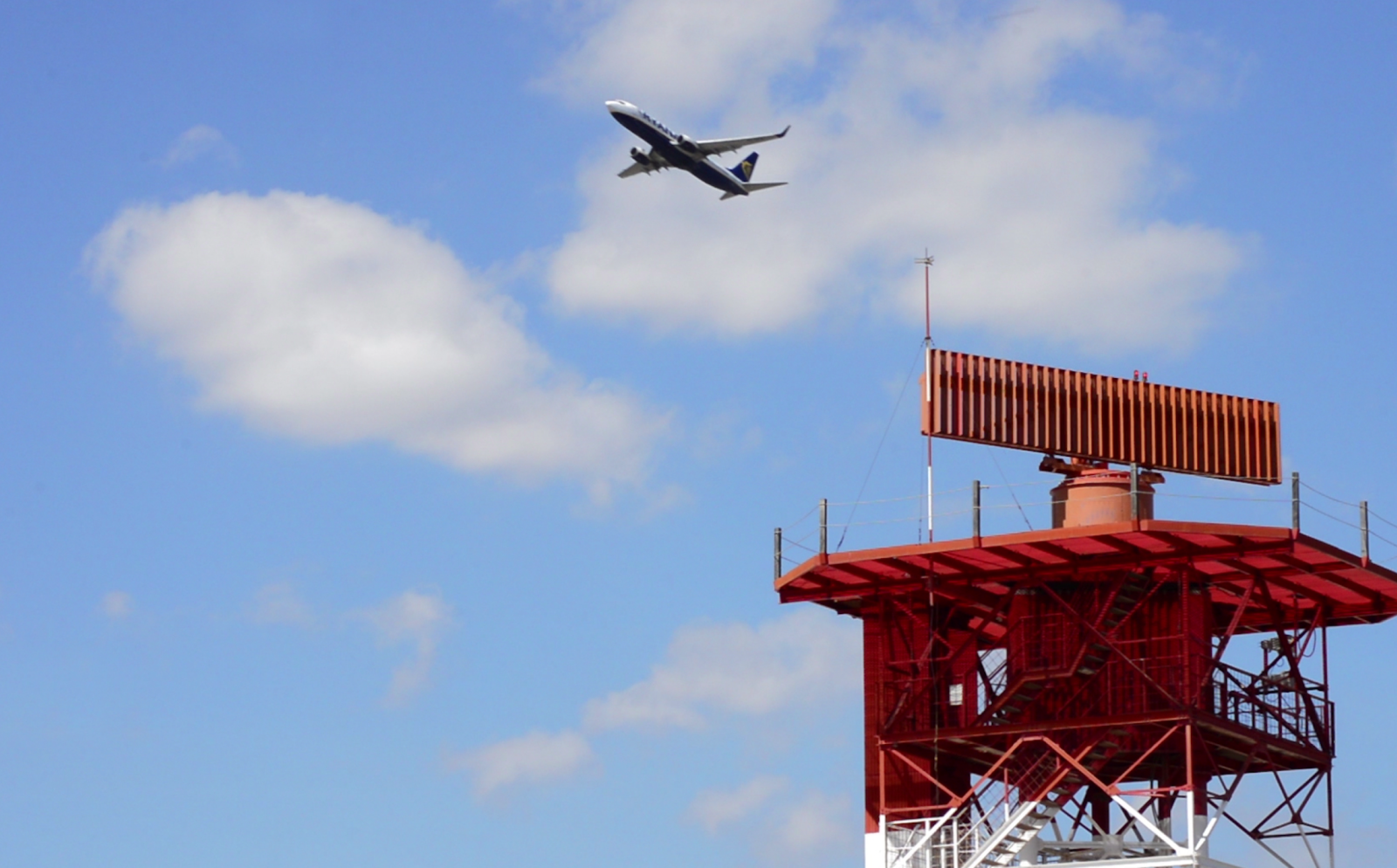 an orange antenna with an airplane in the sky behind it
