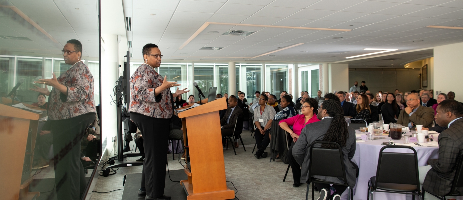 Robbin Chapman stands at a podium and addresses attendees seated at the luncheon. 