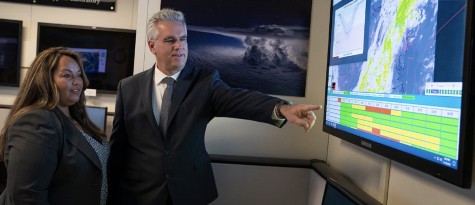 Two researchers stand and point at a screen displaying air traffic control imagery.