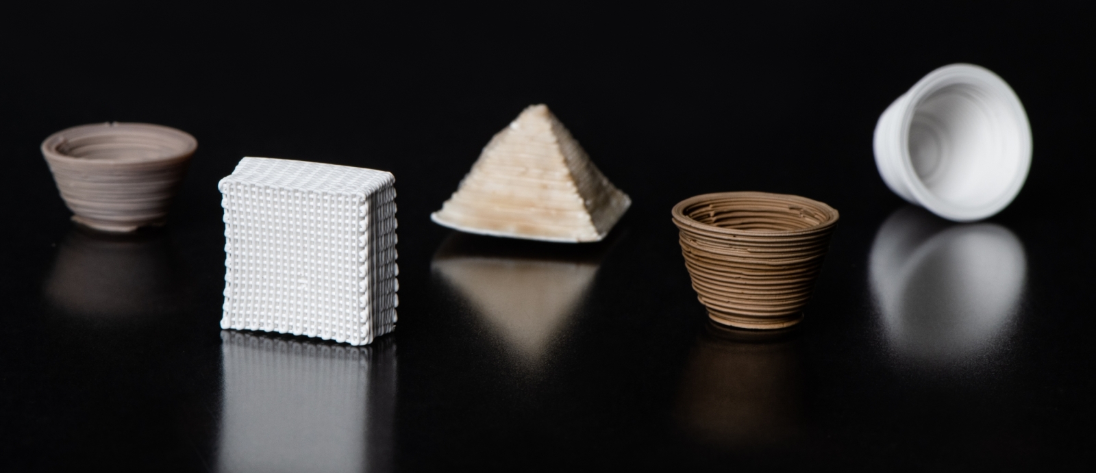 Five small 3D-printed vessels of various colors (white, browns) and shapes (cups, pyramid shapes