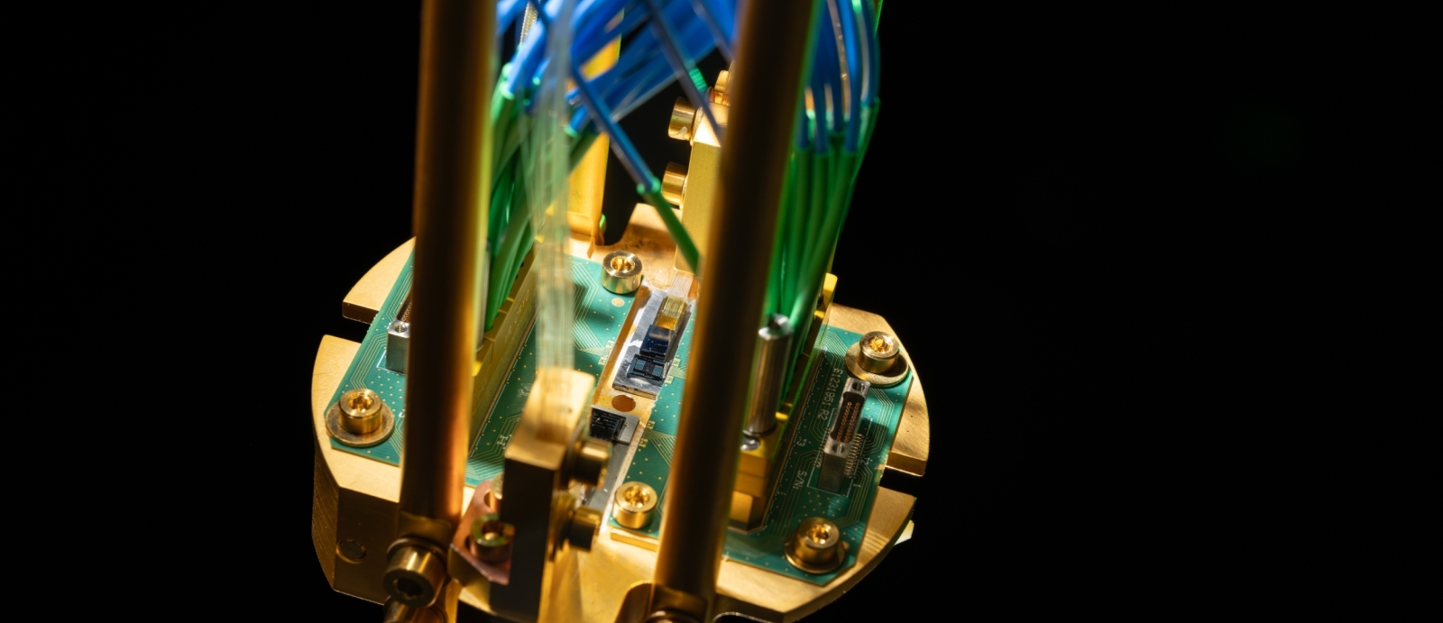 An up-close of a quantum repeater module mounted on a gold-plated copper assembly and connected to green printed circuit boards, with optical fibers routed up.