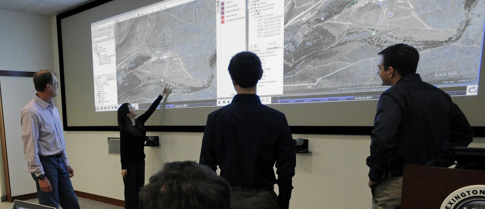 Technical staff members in the Intelligence and Decision Technologies Group review imagery of a location of interest in the maps projected in the PED Lab.