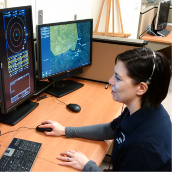 A ground operator sits in front of two computer screens. 