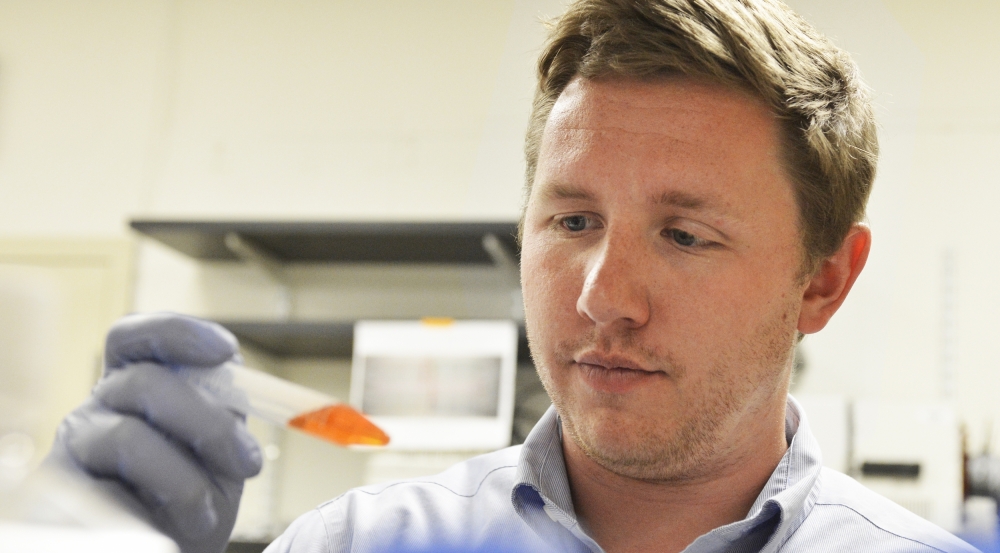 A staff member holds up a test tube filled with orange liquid