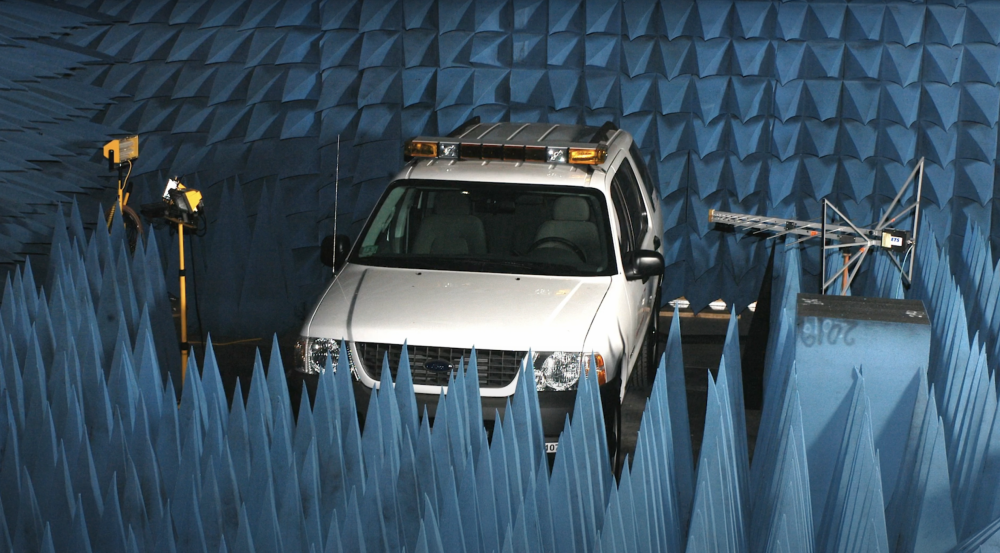 a photo of a car with antennas next to it inside on anechoic chamber (blue foam cones surrounding).