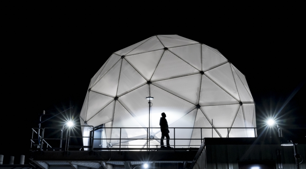 The radome protecting the Multi-Band Test Terminal — a large antenna on an MIT Lincoln Laboratory building rooftop — is shown illuminated at night. 