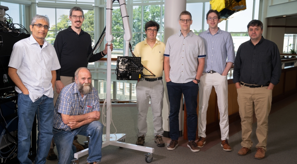 Seven individuals stand with a portable armature holding a laser-based ultrasound system.