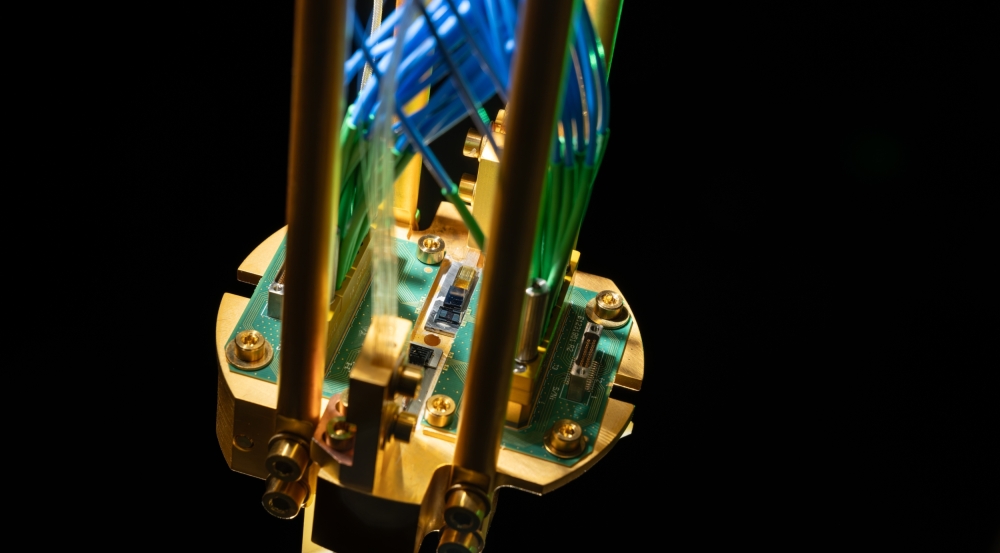 An up-close of a quantum repeater module mounted on a gold-plated copper assembly and connected to green printed circuit boards, with optical fibers routed up.