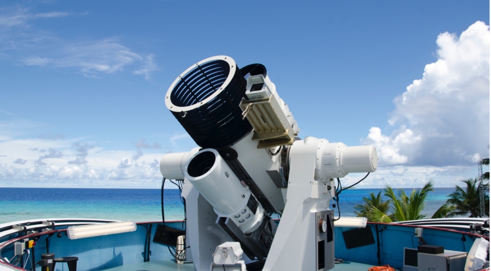 A photograph of a large optical system, with the ocean in the background. 