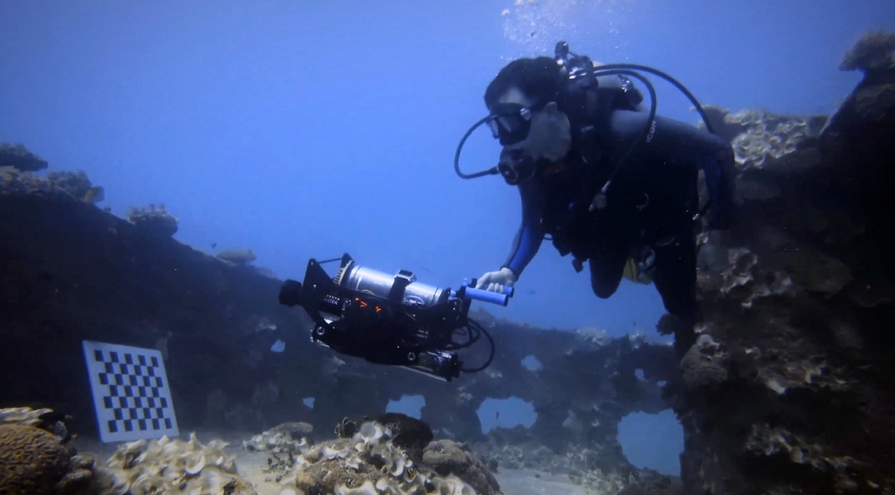 A person swims underwater to map a sunken vessel.