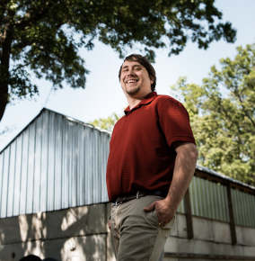 A photo of James Kurdzo outside with a building and tree in background