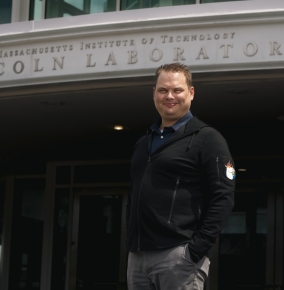A portrait photograph of Joshua Van Hook outside the front entrance of MIT Lincoln Laboratory.