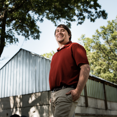 A photo of James Kurdzo outside with a building and tree in background