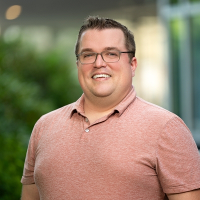 A photo of Derrick McKee smiling, with trees and a building in the background.