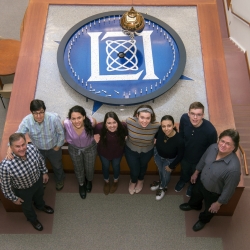 5 students and 3 mentors pose in front the Laboratory's pendulum. 