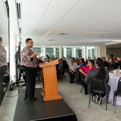 Robbin Chapman stands at a podium and addresses attendees seated at the luncheon. 