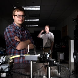 Two men standing in a laboratory with a laser transmitter setup 