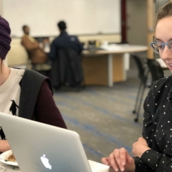 A photo of two women sitting in a classroom on their laptops 