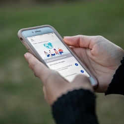 Two hands hold an Iphone; the screen shows the interface of a COVID-monitoring app that reads "No significant exposures"