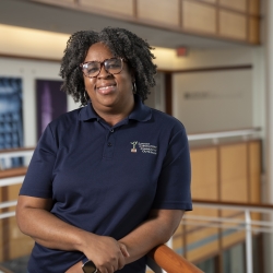 A photo of Chiamaka smiling for a photo, while standing in the lobby of MIT Lincoln Laboratory 