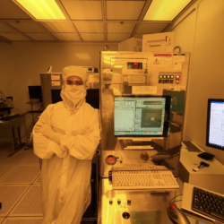 an intern dressed in a "bunny suit" leans against a machine in the microelectronics laboratory.