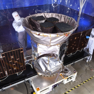 A photo of two scientists inspecting the tess satellite in a cleanroom environment. 