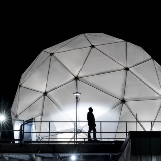 The 38-foot-wide radome protecting the Multi-Band Test Terminal — a large antenna on an MIT Lincoln Laboratory building rooftop — is shown illuminated at night.