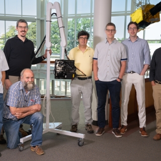 Seven individuals stand with a portable armature holding a laser-based ultrasound system.