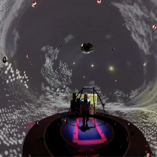 A person walks on a treadmill, surrounded by a domed virtual environment screen