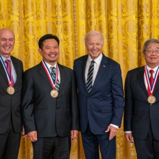 A photo of Eric Swanson, David Huang, and James Fujimoto with President Biden, smiling with medals around their necks.