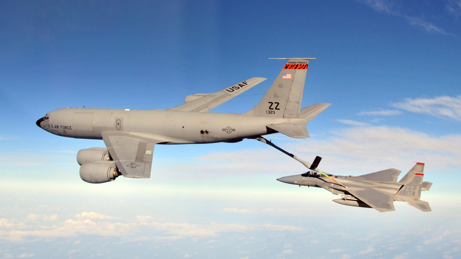 A large KC-135R tanker aircraft refuels an F-15 Eagle aircraft while they in mid air. 