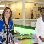 Two scientists stand in a laboratory in front of a green-lit sculpture 