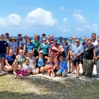 A large group gathers outside near the ocean. 