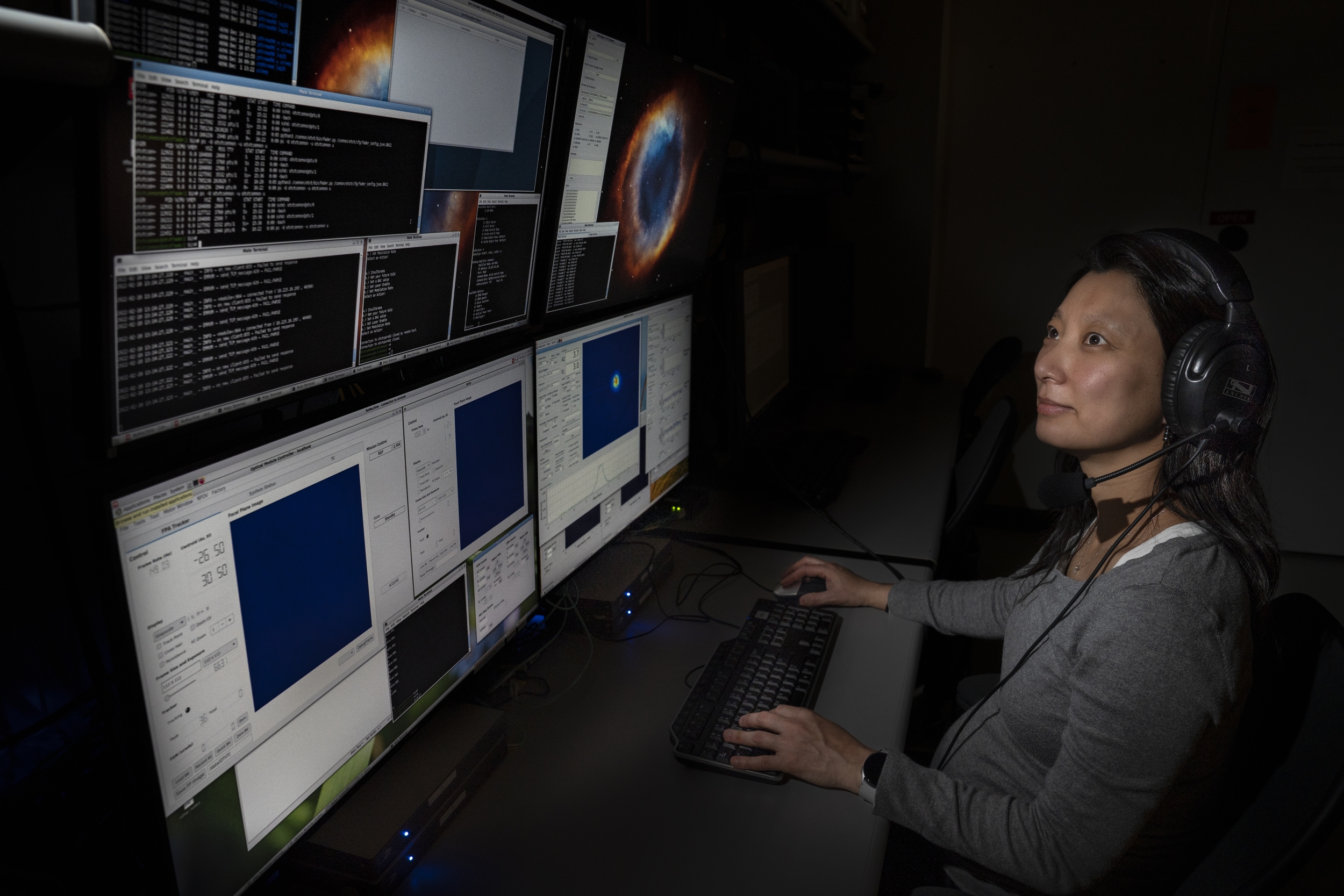 A woman sits looking at several computer screens.